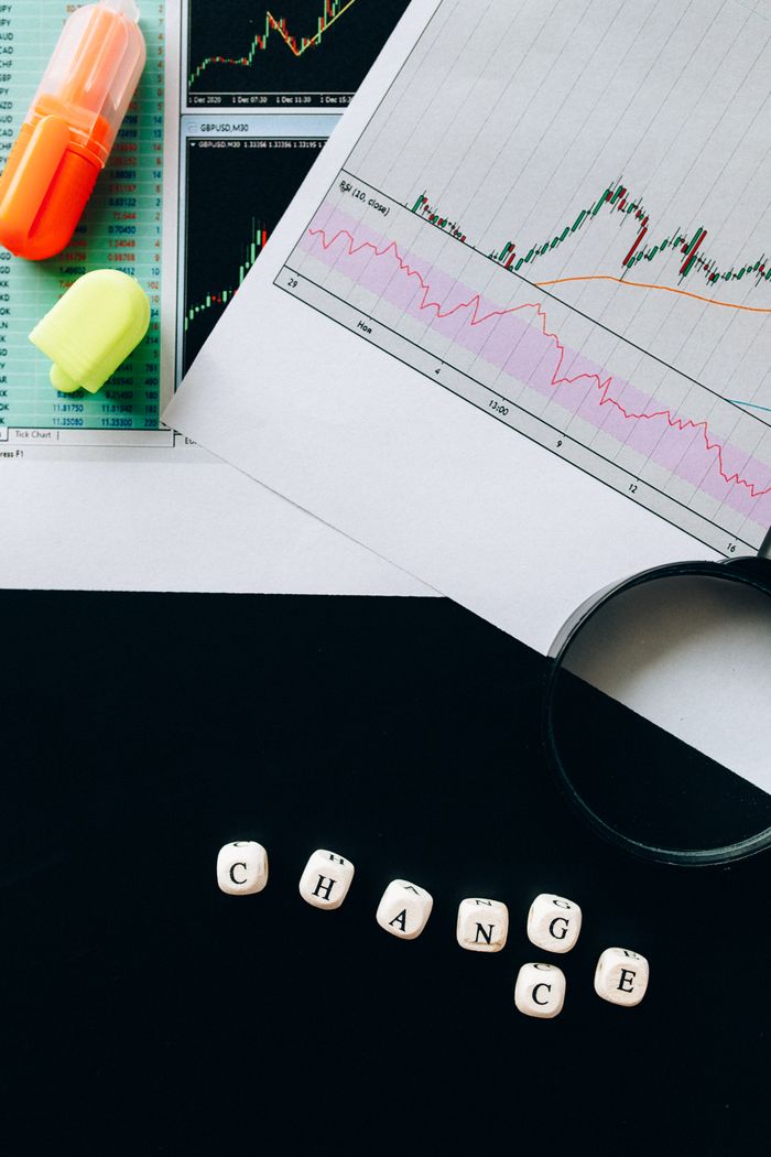 A flat lay image featuring financial charts, highlighters, and dice spelling CHANGE on a black background.